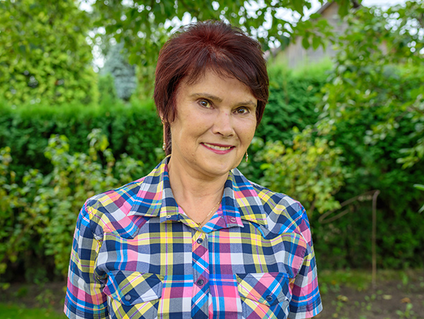 Natural Pharmaceuticals ImuBerin Moteris su trumpais rudos spalvos plaukais ir spalvota languota marškinėliais žalioje sode.